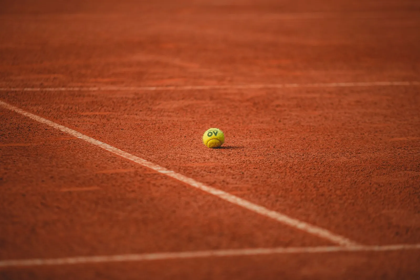 A lone tennis ball rests on a red clay tennis court, highlighting its vibrant texture.