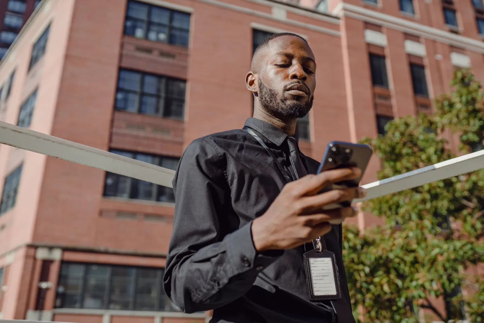Professional man in business attire using smartphone outside office building during the day.