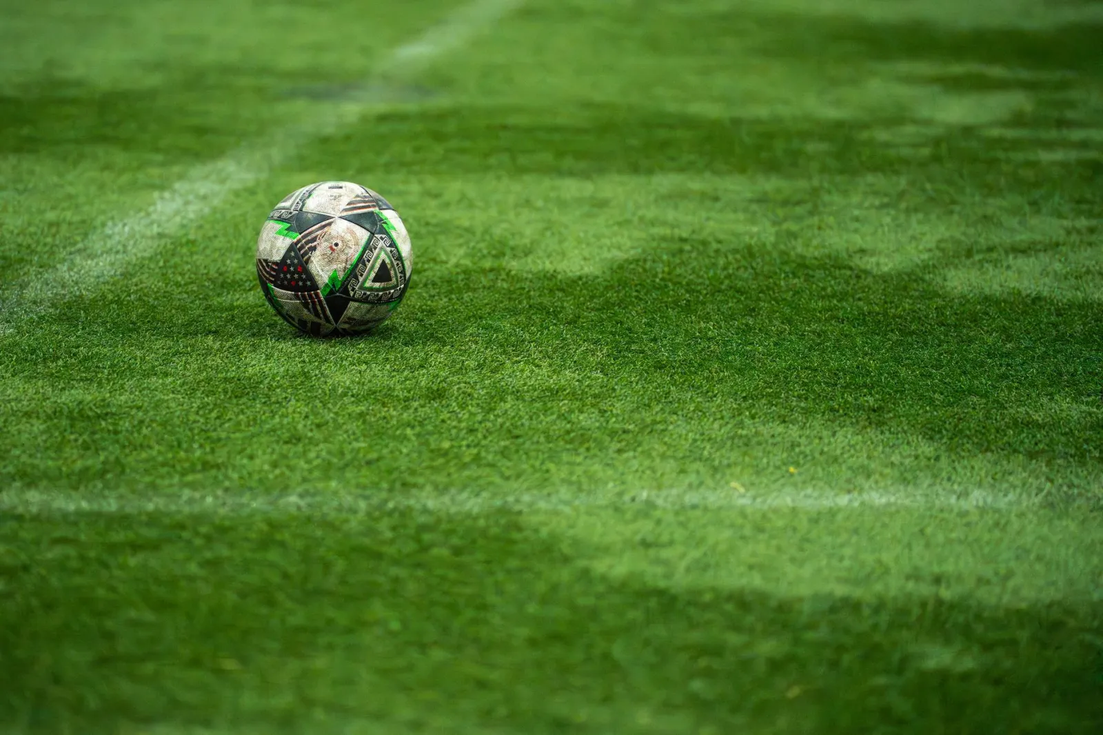 Close-up of a soccer ball resting on a vibrant green turf field, perfect for sports image needs.