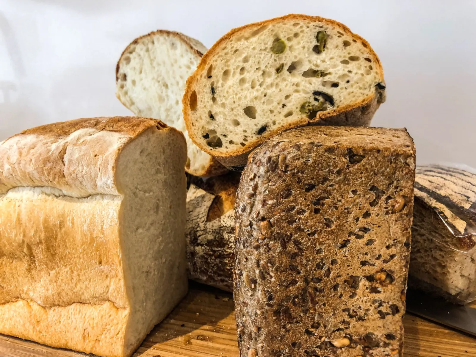 Close-up of various artisan bread loaves and slices on a wooden board, featuring fresh and baked textures.