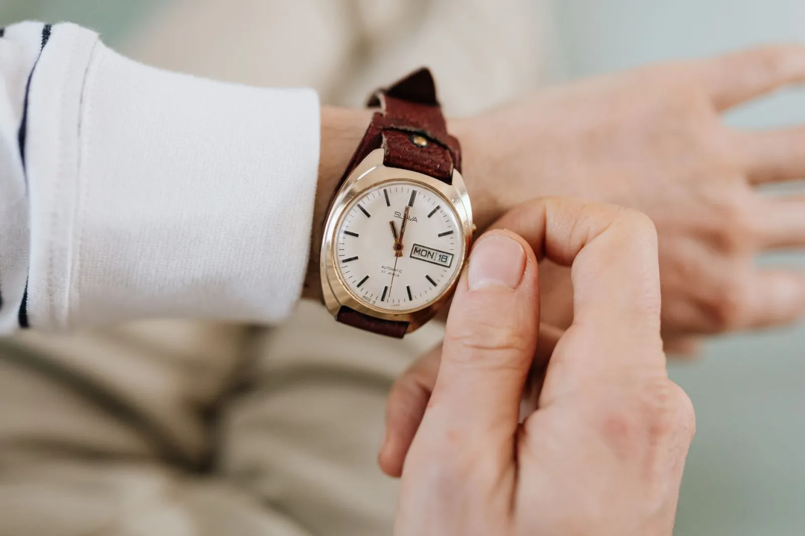 A close-up of a person adjusting a vintage brown leather strap analog wristwatch.